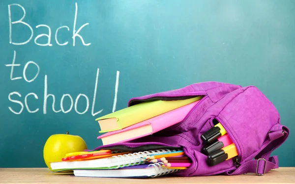 Purple backpack with school supplies on wooden table on green desk background ロイヤリティフリーのストック写真