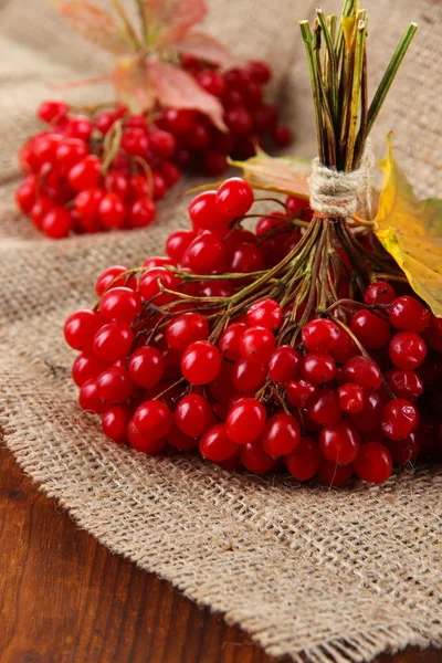 Red berries of viburnum on sackcloth napkin, on wooden background — Stock Photo, Image