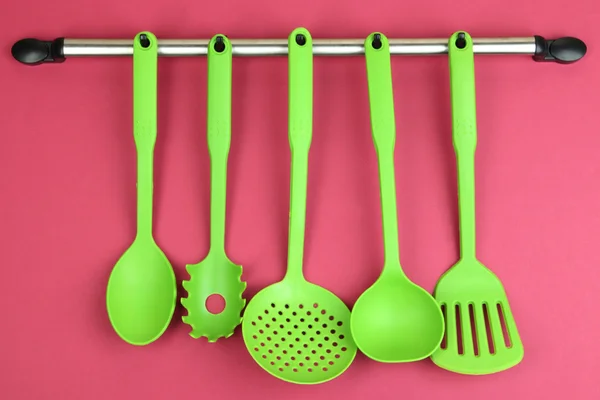 Plastic kitchen utensils on silver hooks on red background — Stock Photo, Image