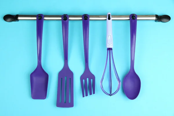 Plastic kitchen utensils on silver hooks on blue background — Stock Photo, Image