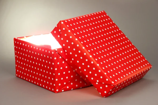 Gift box with bright light on it on grey background — Stock Photo, Image