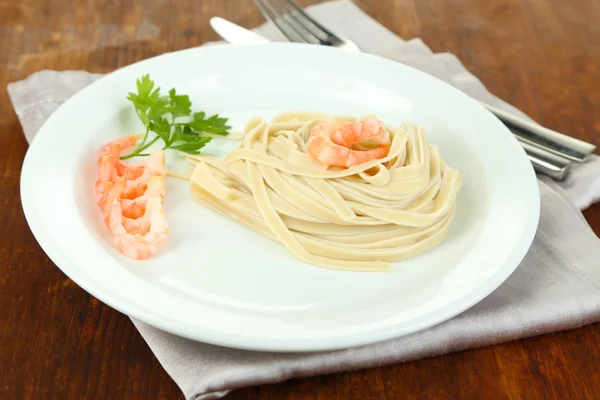 Pasta met garnalen op witte plaat, op houten achtergrond — Stockfoto