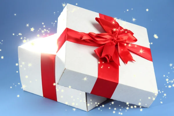 Gift box with bright light on it on blue background — Stock Photo, Image