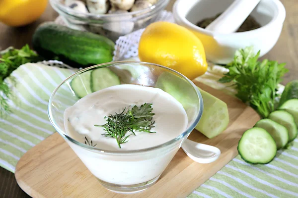 Komkommer yoghurt in glazen kom, op kleur servet, op houten achtergrond — Stockfoto