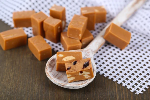 Many toffee in wooden spoon on napkin on wooden table — Stock Photo, Image