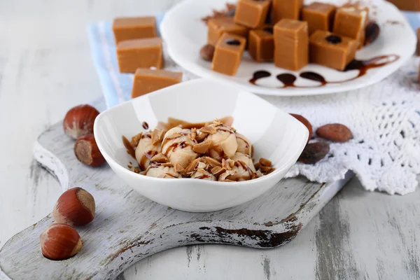 Many toffee on plate and in bowl on napkin on board on wooden table — Stock Photo, Image