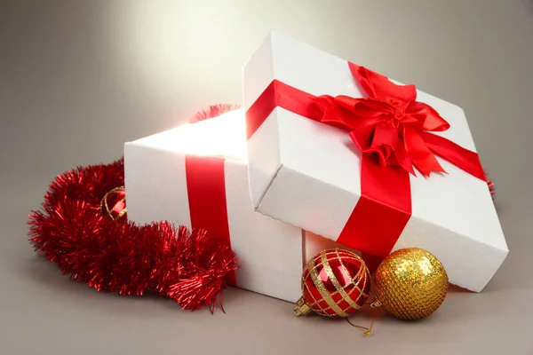 Gift box with bright light on it on grey background — Stock Photo, Image