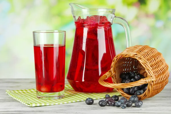 Pitcher and glass of compote on napkin on wooden table on nature background — Stock Photo, Image