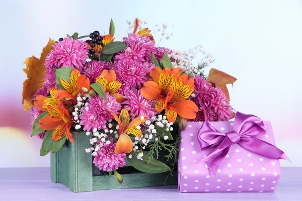 Flowers composition in crate with present on table on bright background