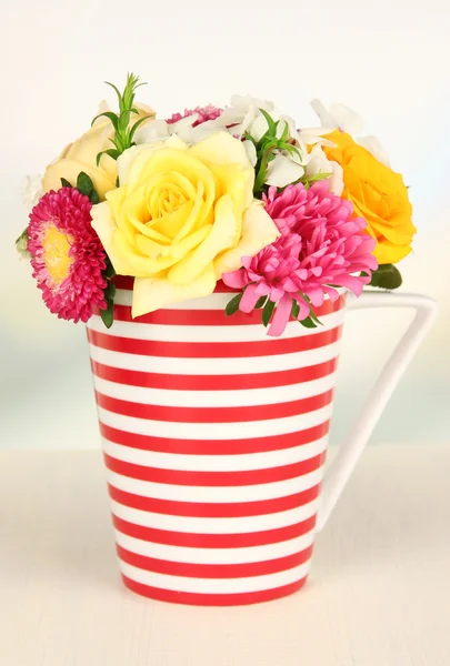 Beautiful bouquet of bright flowers in color mug, on wooden table, on bright background — Stock Photo, Image