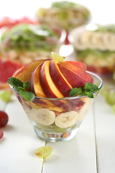 Salada de frutas saborosas em tigela de vidro, na mesa de madeira branca — Fotografia de Stock