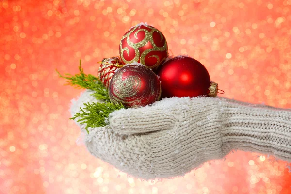 Mãos femininas em mitenes bolas de árvore de Natal, em fundo de cor — Fotografia de Stock