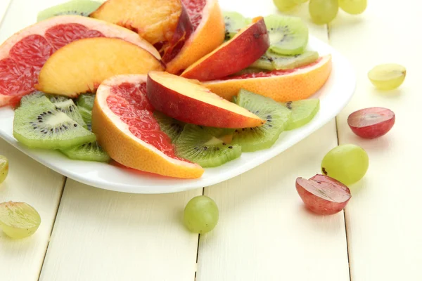 Surtido de frutas en rodajas en plato, sobre mesa de madera blanca — Foto de Stock