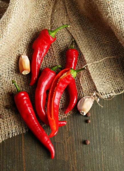 Red hot chili peppers and garlic, on sackcloth, on wooden background — Stock Photo, Image