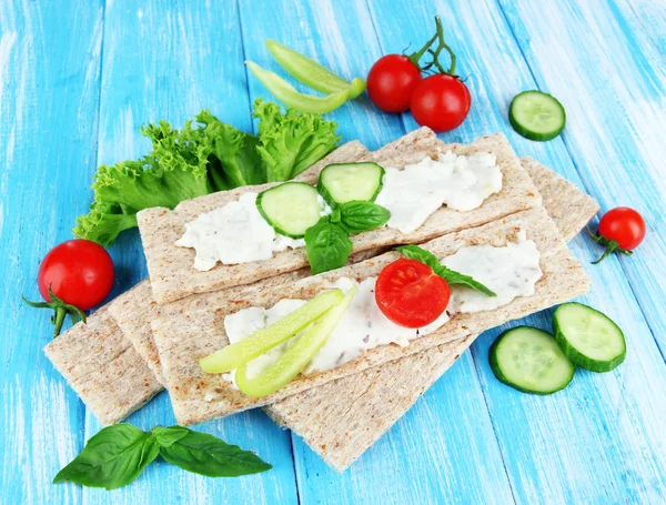 Tasty crispbreads with vegetables on blue wooden background — Stock Photo, Image