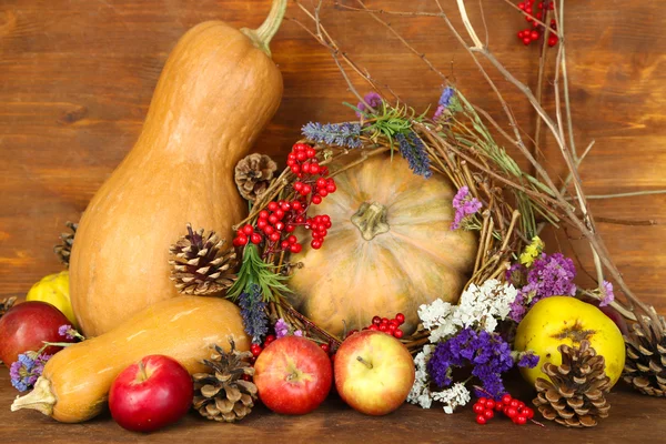 Composition automnale de pommes, citrouilles, fleurs et branches sèches sur table en bois sur fond en bois — Photo