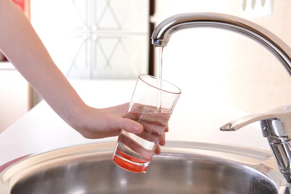 Hand holding glass of water poured from kitchen faucet — Stock Photo, Image