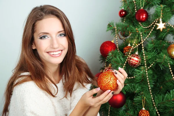 Mooi meisje in de buurt van kerstboom met bal — Stockfoto