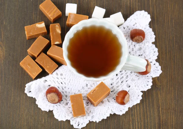 Many toffee and cup of tea on napkin on wooden table — Stock Photo, Image