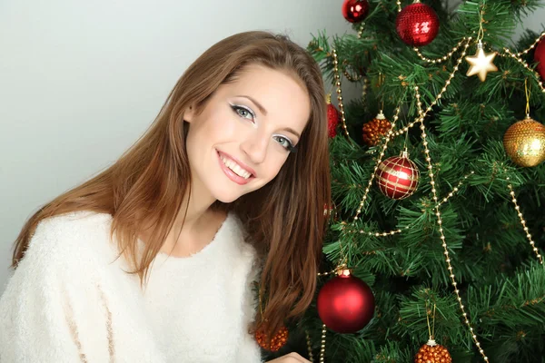 Beautiful smiling girl sitting near Christmas tree in room Stock Picture