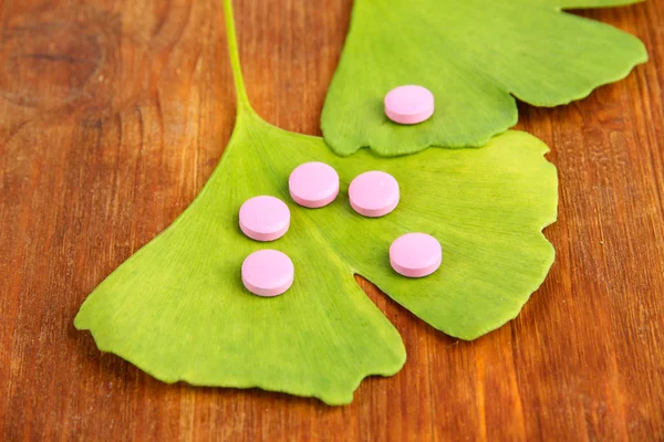 Ginkgo biloba leaves and pills on wooden background — Stock Photo, Image