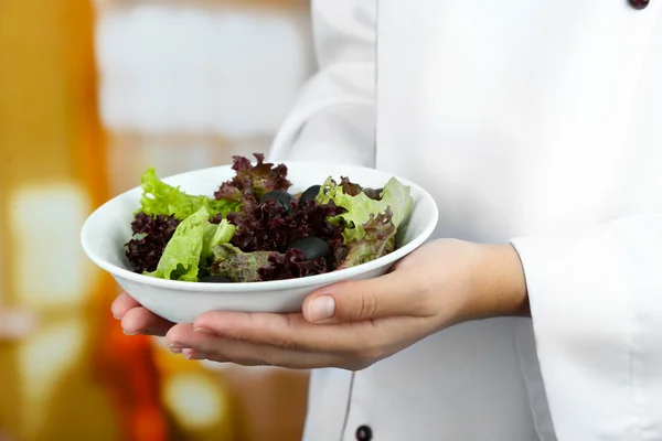 Салат в миске в руках повара на ярком фоне — стоковое фото