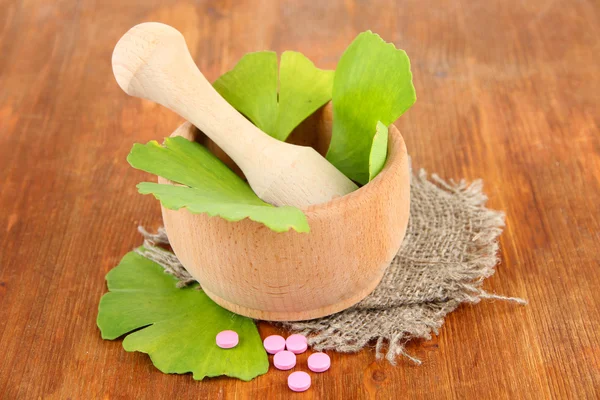 Ginkgo biloba leaves in mortar and pills on wooden background — Stock Photo, Image