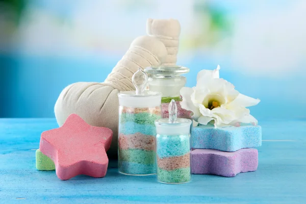 Aromatic salts in glass bottles and herbal compress balls for spa treatment, on blue background — Stock Photo, Image