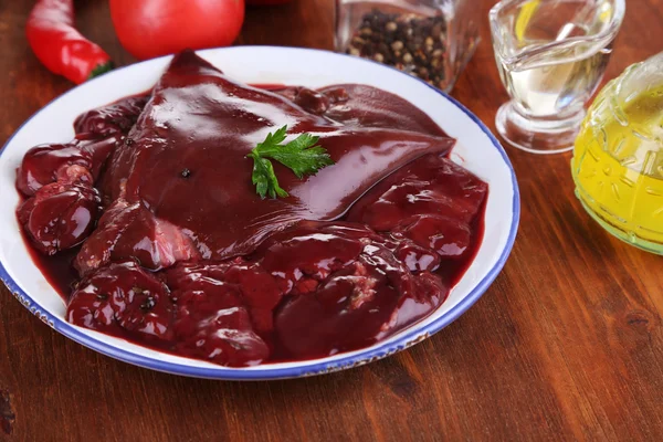 Hígado crudo en plato con especias y condimentos en primer plano de mesa de madera —  Fotos de Stock