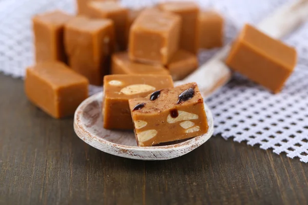 Many toffee in wooden spoon on napkin on wooden table — Stock Photo, Image
