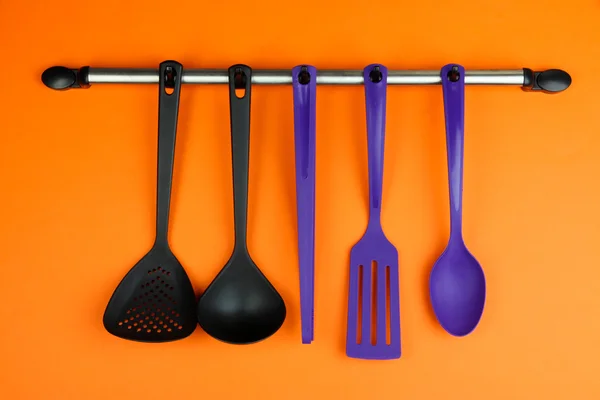 Utensílios de cozinha de plástico em ganchos de prata no fundo laranja — Fotografia de Stock