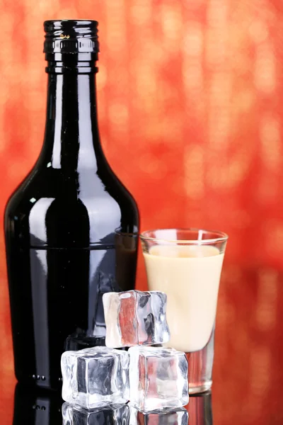 Baileys liqueur in bottle and glass on red background — Stock Photo, Image