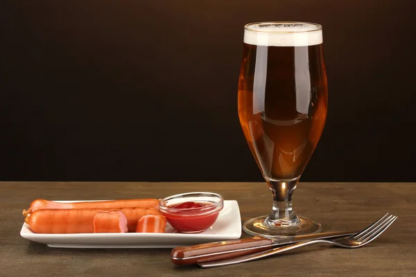 Cerveja e salsichas grelhadas em mesa de madeira sobre fundo marrom — Fotografia de Stock