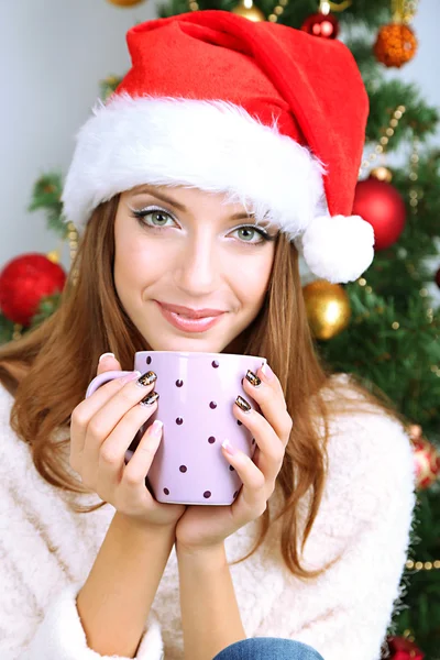 Krásná usměvavá dívka u vánočního stromu s cup — Stock fotografie