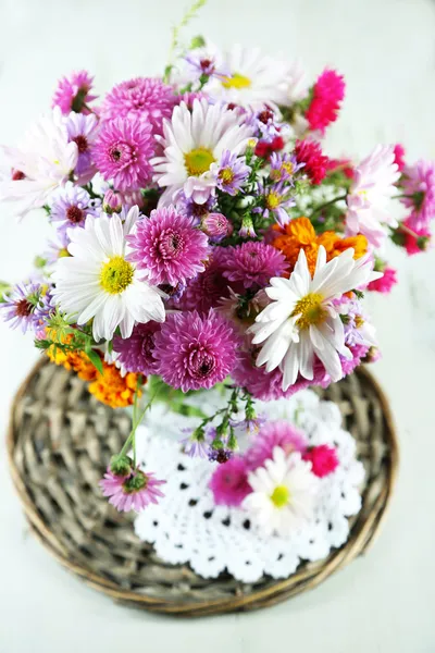 Дикие цветы в стеклянной вазе на плетеном подносе на деревянном столе — стоковое фото