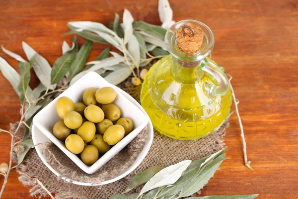 Olives in bowl with branch on sackcloth on wooden table — Stock Photo, Image
