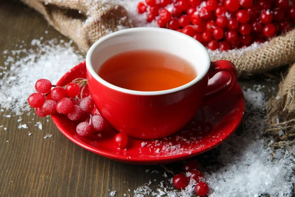 Stilleven met planten van viburnum thee in cup, bessen en sneeuw, op rouwgewaad servet, op houten achtergrond — Stockfoto