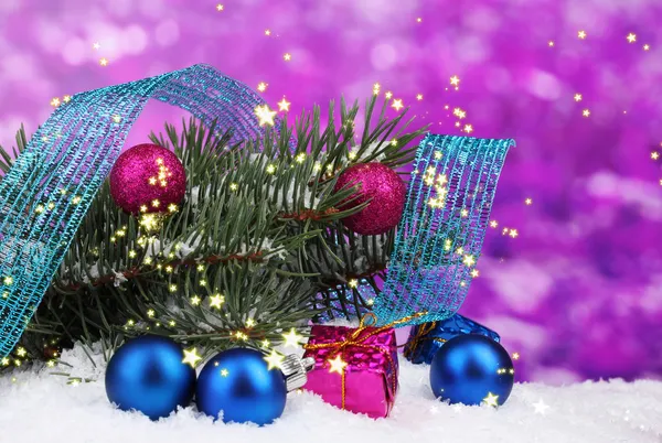 Groene kerstboom met speelgoed en lint in de sneeuw op paars — Stockfoto