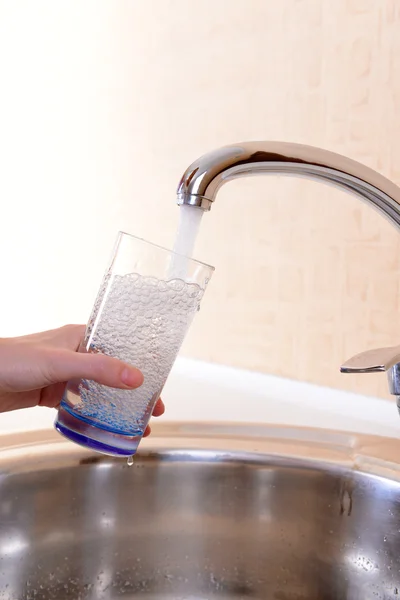 Hand som håller glas vatten hälls från köksblandare — Stockfoto