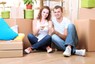 Young couple celebrating moving to new home sitting among boxes clipart