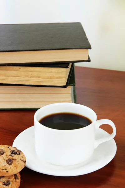 Xícara de café com biscoitos e livros em mesa de madeira sobre fundo brilhante — Fotografia de Stock