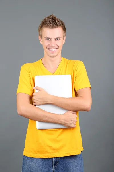 Pohledný mladý muž s notebookem na šedém pozadí — Stock fotografie