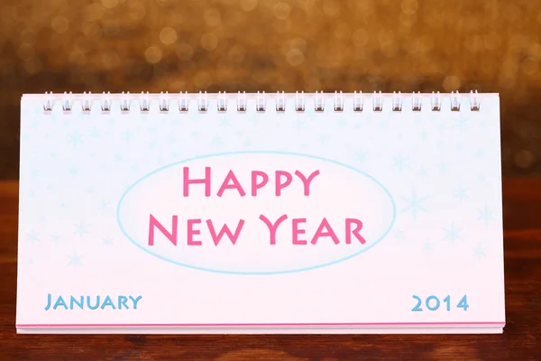 New jaarkalender op houten tafel, op glanzende gouden achtergrond — Stockfoto