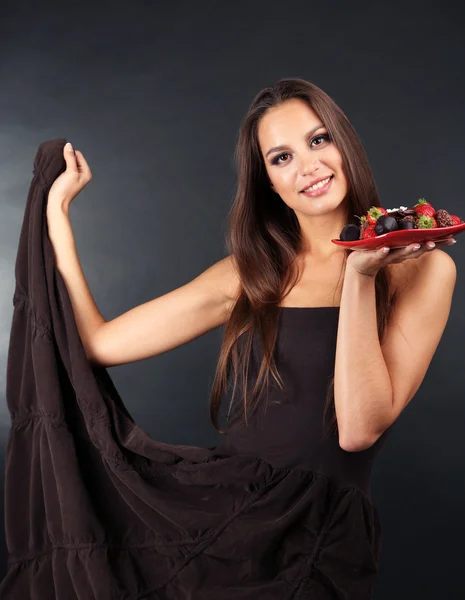 Retrato de una hermosa joven con dulces de chocolate en el plato sobre fondo gris — Foto de Stock