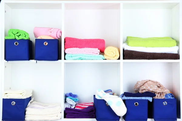 Blue textile boxes with towels and clothes in white shelves — Stock Photo, Image