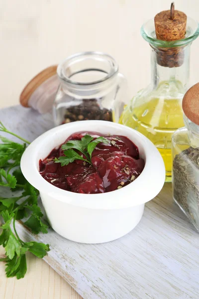 Raw liver in bowl with spices and condiments on wooden table close-up — Stock Photo, Image