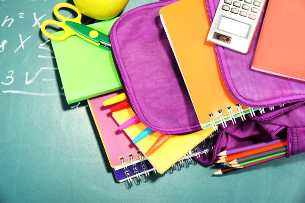 Фіолетовий рюкзак з шкільними приладдям на фоні зеленого столу — стокове фото