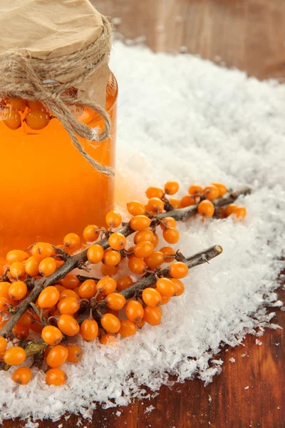 Branches of sea buckthorn with jam and snow on wooden background — Stock Photo, Image