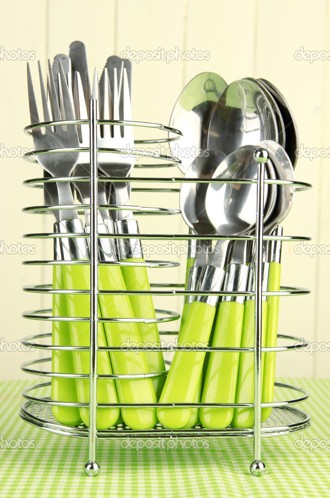 Knives, forks and spoons in metal stand on tablecloth on beige