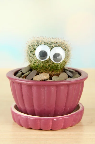 Cactus in flowerpot with funny eyes, on wooden table — Stock Photo, Image